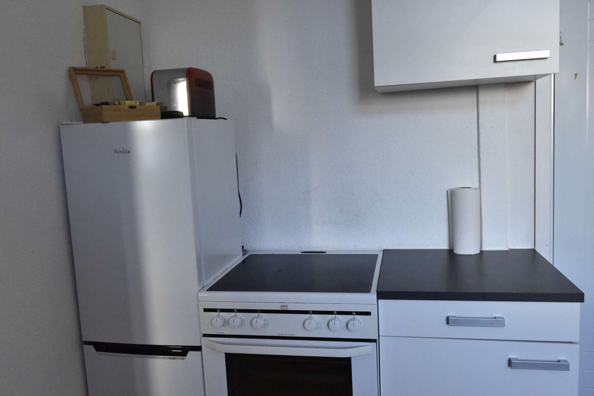 A compact kitchen with a refrigerator, stove, oven, and a small cabinet.