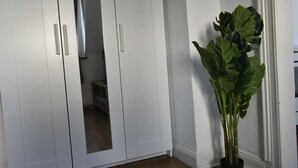 Une armoire blanche avec une porte miroir, une plante en pot et un mur blanc.