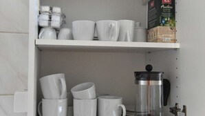 Une étagère de cuisine avec des tasses blanches, une machine à café et une boîte de café Melitta.