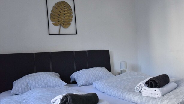 Une chambre d’hôtel avec un grand lit, deux oreillers, une décoration représentant une feuille encadrée et une serviette pliée posée sur le lit.