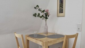 Une table de salle à manger en bois, accompagnée de deux chaises, d’un vase rempli de fleurs et de deux verres.