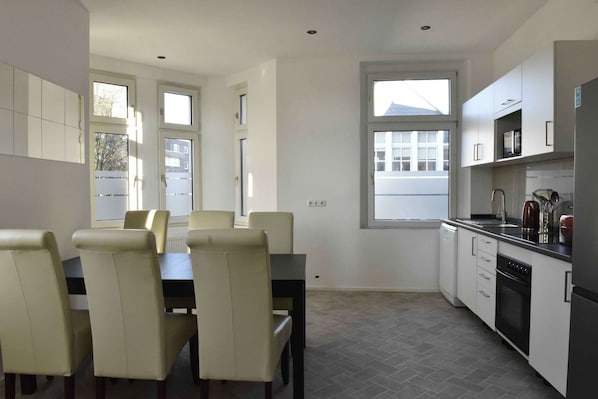 A modern kitchen with white cabinets, a dining table with chairs, and a window.