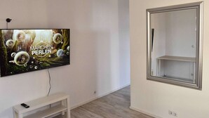 Une pièce avec un téléviseur fixé au mur qui diffuse l’émission « MARCHEN PERLEN » et un banc blanc.