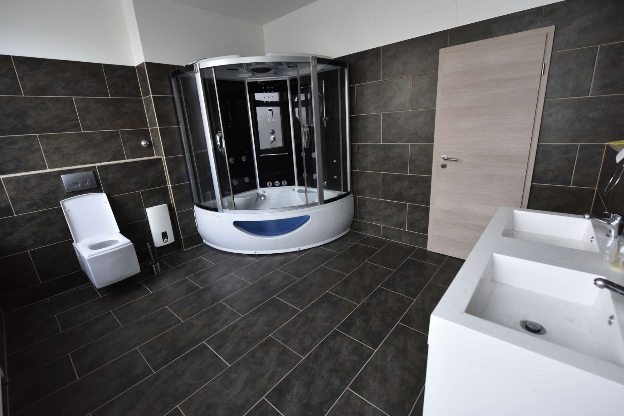 Et moderne badeværelse med jacuzzi med glasvægge, et separat toilet og en stor vask.