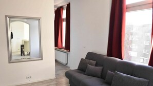 Un salon avec un canapé gris, des rideaux rouges, un miroir et une vue sur l’extérieur.