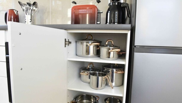 Un meuble de cuisine contenant des casseroles et des poêles en acier inoxydable.