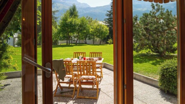 A patio with a table and chairs, a view of a green lawn, and mountains in the background. - Chesa Dal Luf B1 by Interhome (Silvaplana-Surlej)