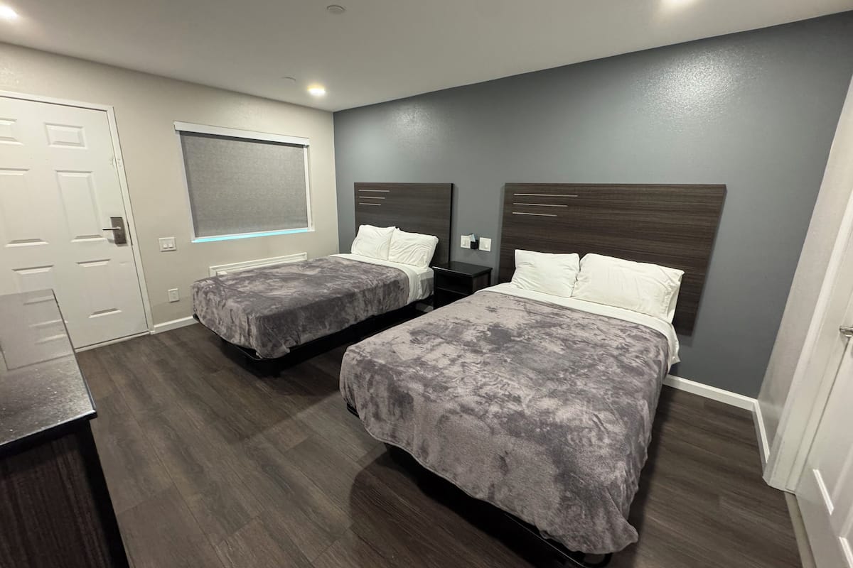 A hotel room with two beds, a desk, and a window with blinds.