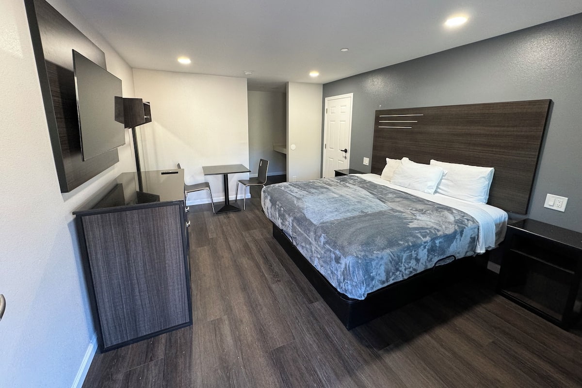 A modern hotel room with a large bed, a desk, a chair, and a TV mounted on the wall.