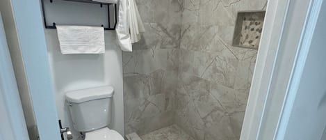 A bathroom with a toilet, a shower with a glass door, and a towel rack with folded towels.