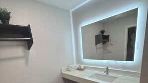 Een moderne badkamer met een wit wastafel, een grote spiegel en een houten bankje.