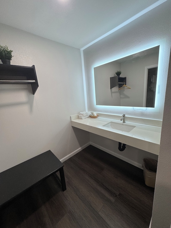 A modern bathroom with a white sink, a large mirror, and a wooden bench.