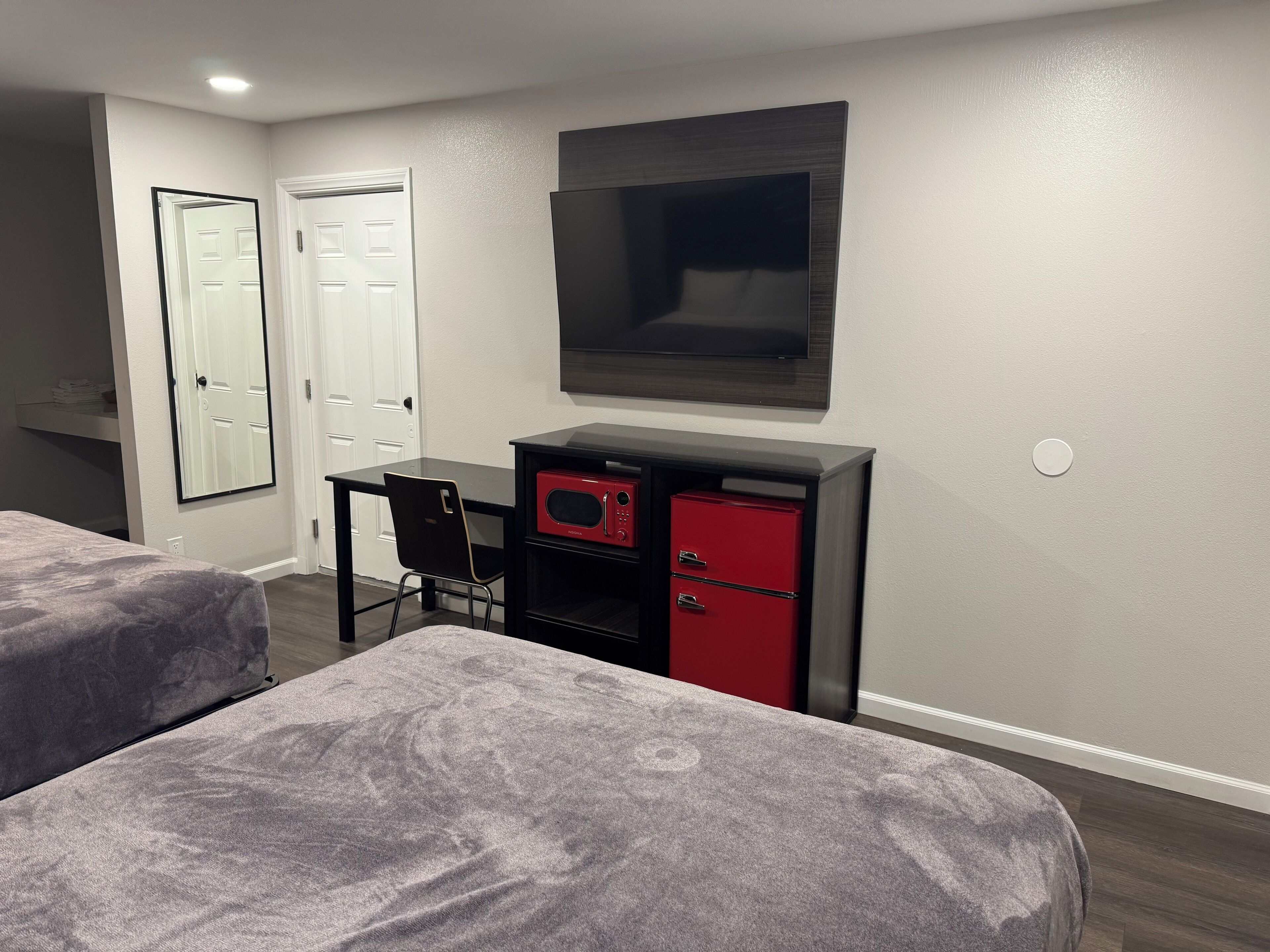 A hotel room with two beds, a desk with a chair, a TV, and a red storage unit.