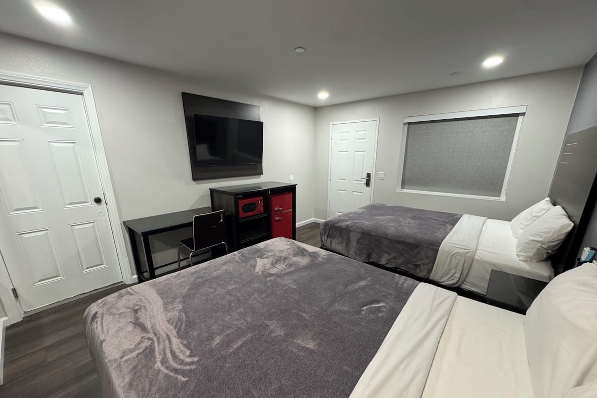 A hotel room with two beds, a TV mounted on the wall, a desk with a chair, and a wardrobe.