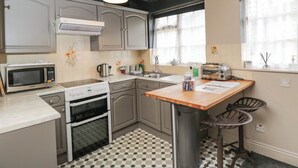 A kitchen with a microwave, stove, sink, and a small bar area with stools. - Paddock Cottage (Malmesbury)