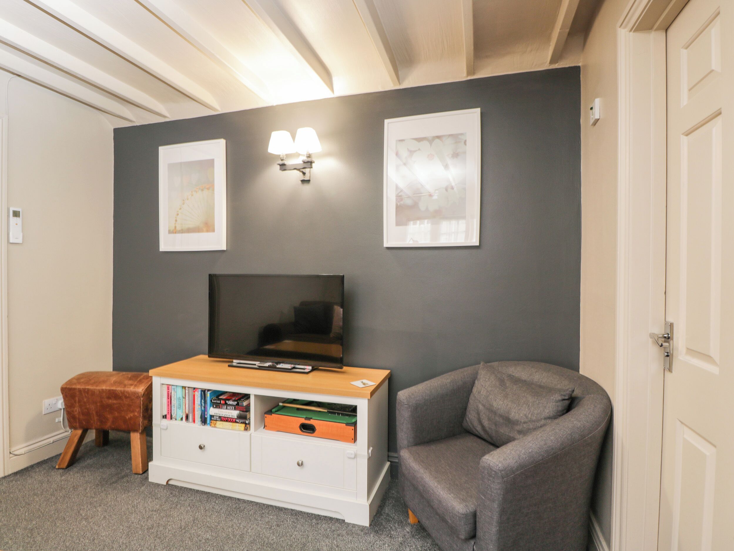 A room with a grey wall, a white cabinet with books, a grey armchair, and a flat-screen TV.