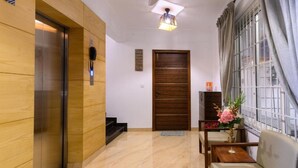 A modern interior with a wooden elevator, a wooden door, a small table with a vase of flowers, and a seating area by a window. - Lotus & Orchid Villas by Ramnath Homes (Alto de Porvorim)