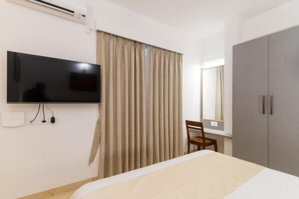 Une chambre d’hôtel avec un lit, un téléviseur fixé au mur, une armoire et une fenêtre avec des rideaux.