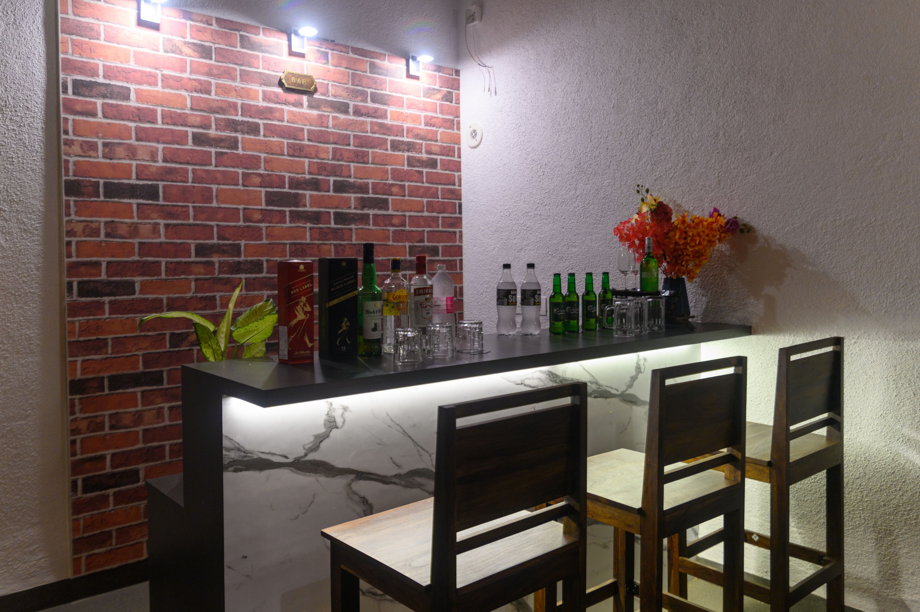 Uma área de bar com bancada de mármore, cadeiras de madeira e parede de tijolos.