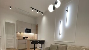 Una sala de estar moderna con un sofá color beige, dos mesas de centro negras y un área de cocina con armarios blancos y un microondas.