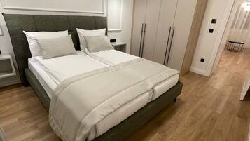 A modern bedroom with a large bed, wooden flooring, and built-in wardrobes.