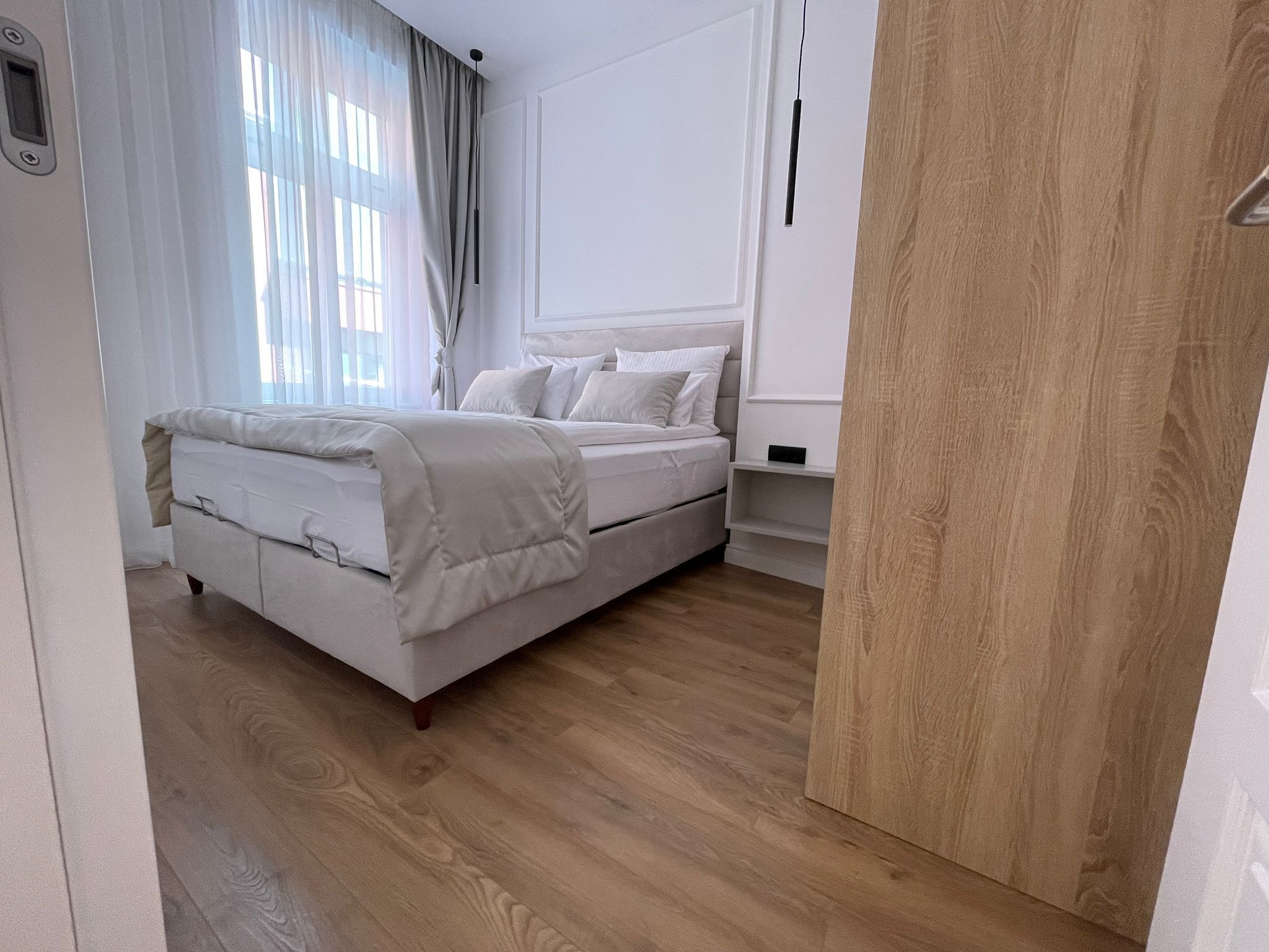 Ein Schlafzimmer mit einem Bett, Holzboden, einem weißen Wandschrank und einem Fenster mit Vorhängen.