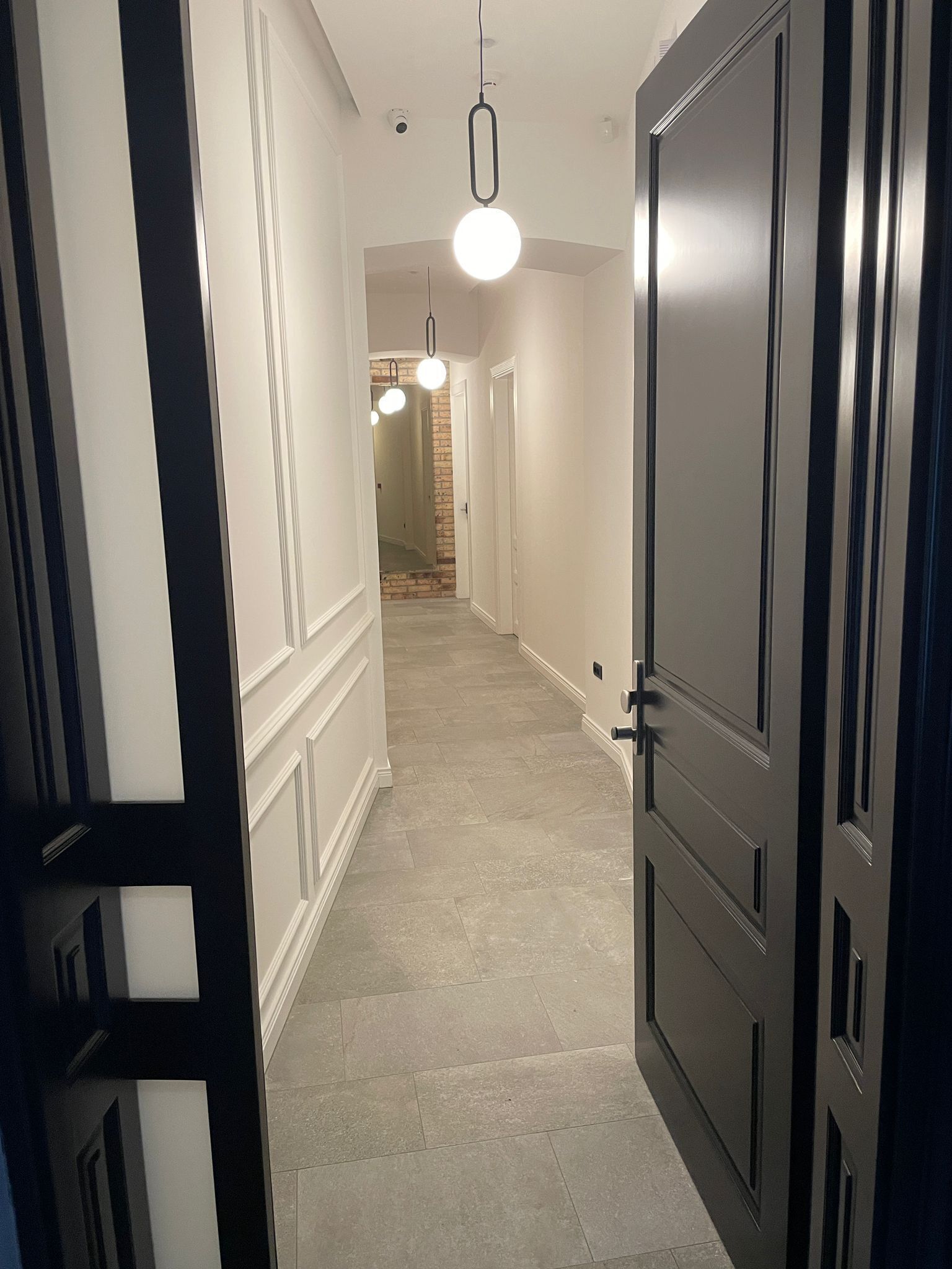 A hallway with a door on the right, a light fixture above, and a brick wall at the end.
