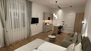A modern bedroom with a large bed, a sofa, a small table, and a kitchen area in the background. - Central Apartments Sarajevo (Sarajevo)