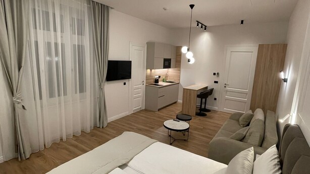 Un dormitorio moderno con una cama grande, un sofá, una mesita y una cocina al fondo.