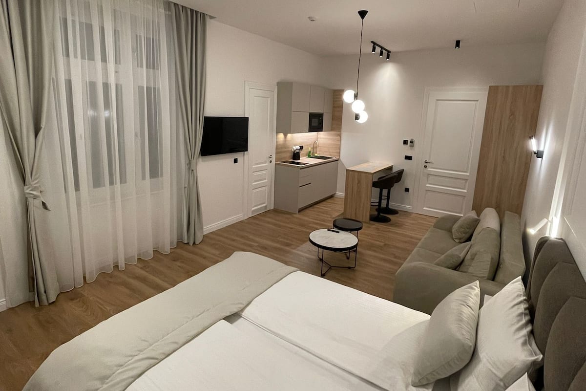 Et moderne soveværelse med en stor seng, en sofa, et lille bord og et køkkenområde i baggrunden.