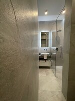 Un baño moderno con ducha envuelta en vidrio, un espejo grande y un lavamanos con estante para toallas.
