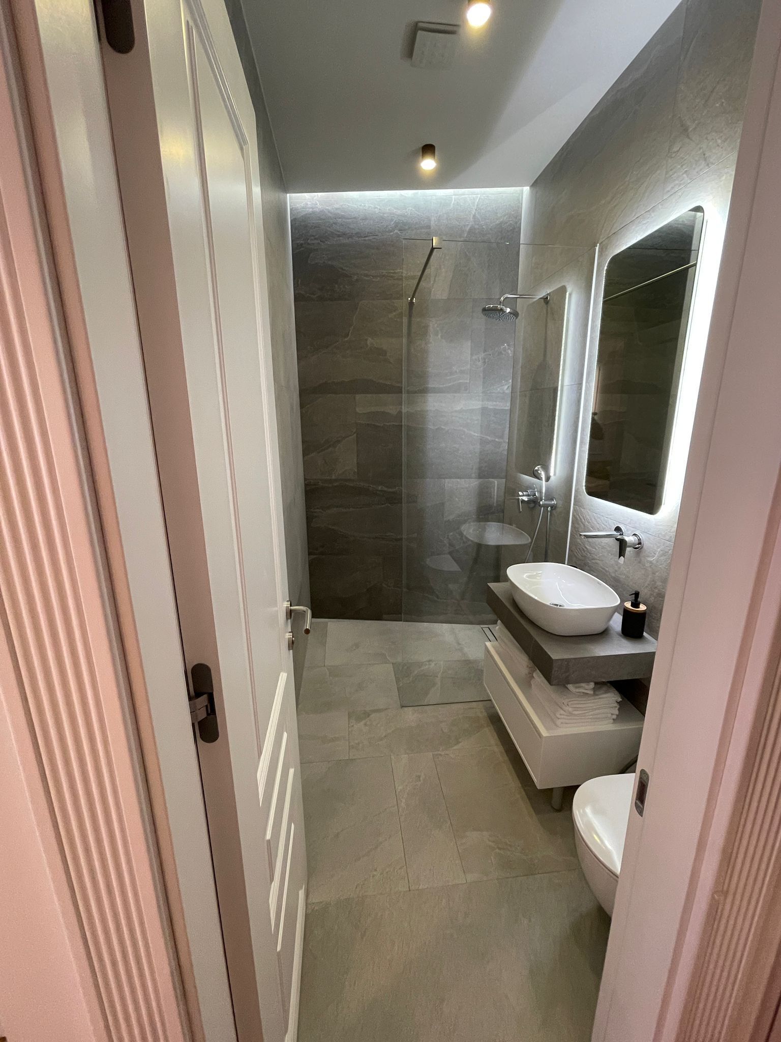 A modern bathroom with a glass-enclosed shower, a large mirror, and a white sink.