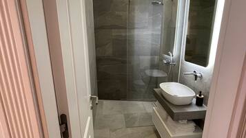 A modern bathroom with a glass-enclosed shower, a large mirror, and a white sink.