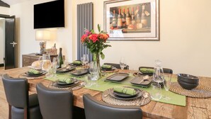 Un coin repas avec une table en bois dressée pour six personnes, entourée de chaises noires. Un vase rempli de fleurs est placé au centre.