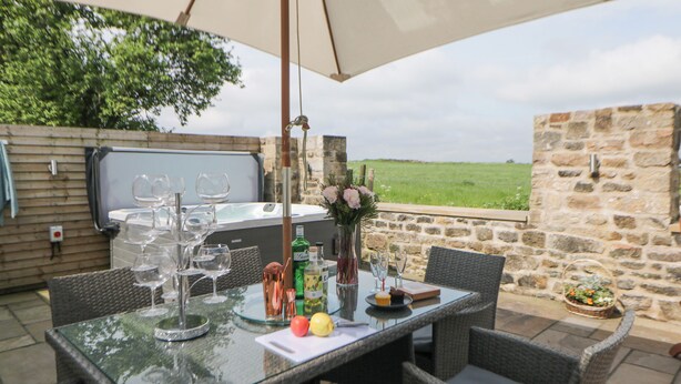 Un espace extérieur aménagé pour les repas, avec des chaises en osier, une table en verre et un jacuzzi en arrière-plan.
