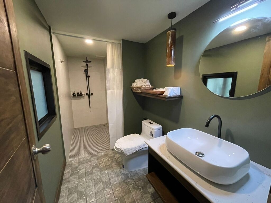 Een badkamer met douche, toilet, wastafel en spiegel.