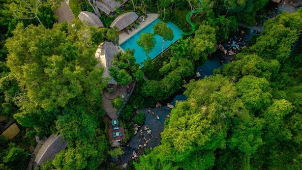 Eine Vogelperspektive zeigt ein Resort mit einem Schwimmbad, einem kleinen Steg und üppiger umliegender Bepflanzung.