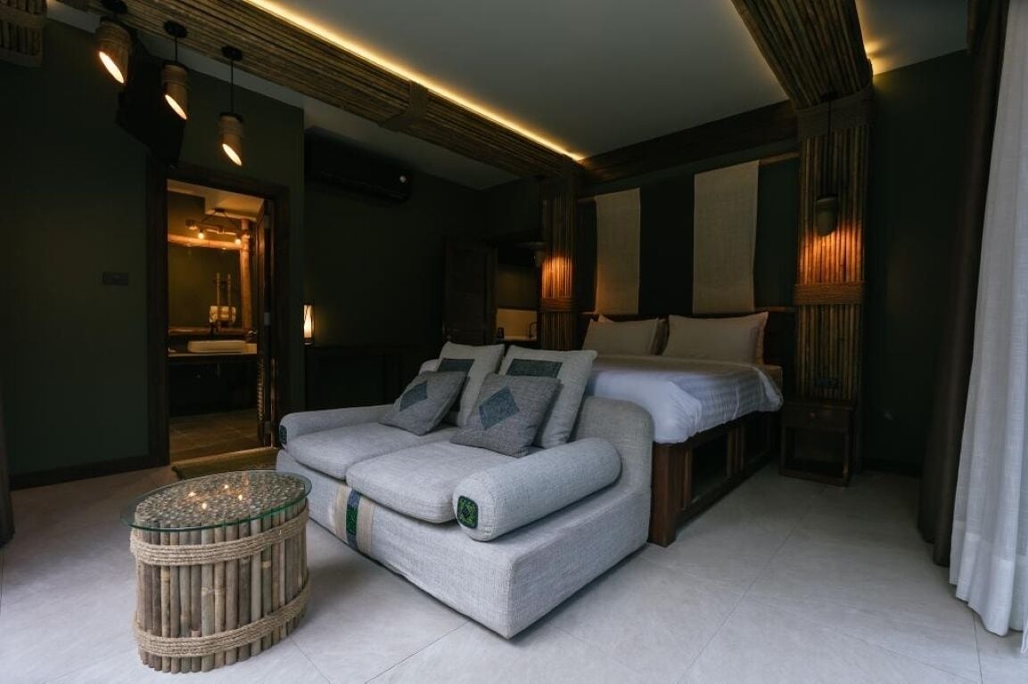 Un dormitorio moderno con una cama, una mesita de noche, un sofá y un baño visible a través de una puerta abierta.