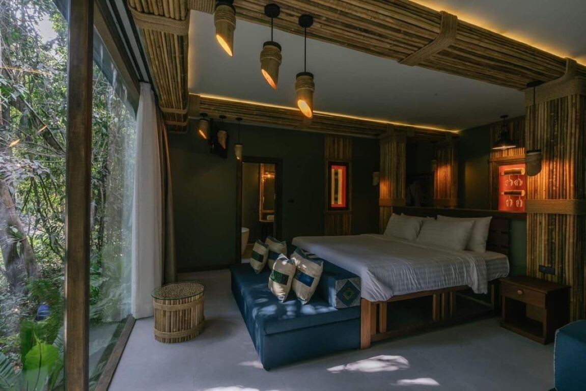 Ein Schlafzimmer mit einem großen Bett, einer Bank und einem Fenster mit Blick auf Grünflächen.