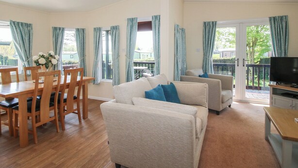 Ampla sala de estar com mesa de jantar, cadeiras, sofás, televisão e janelas grandes com cortinas.