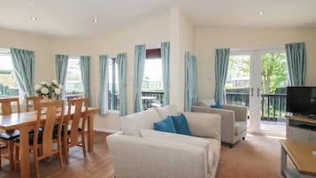 A spacious living area with a dining table, chairs, sofas, a TV, and large windows with curtains.