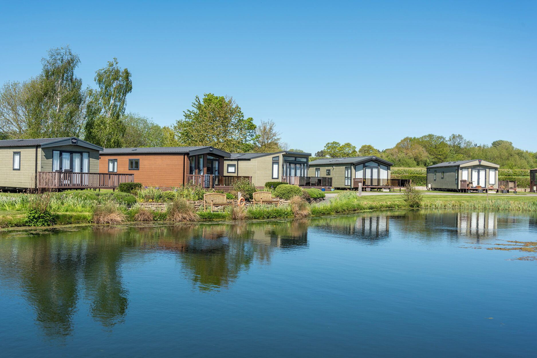 A row of mobile homes by a calm lake with a clear sky.