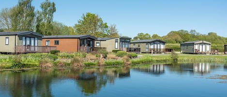 A row of mobile homes by a calm lake with a clear sky.