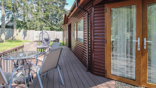A wooden deck with a glass door, outdoor furniture, and a swing chair. - Foxglove (Leominster)