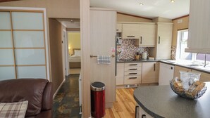 A compact kitchen with a dining area, a trash bin, and a small island with a basket. - Foxglove (Leominster)