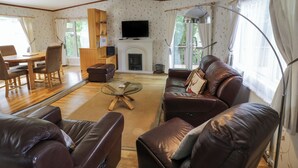 A living room with a fireplace, leather sofas, a dining table with chairs, and a TV mounted on the wall. - Foxglove (Leominster)