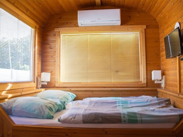 Habitación de cabaña de madera con una cama, una ventana con persianas, aire acondicionado y un calentador de pared.