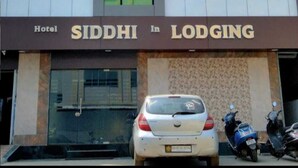 Ein Hotel namens 'SIDDHI In Lodging' mit einer modernen Fassade, großen Fenstern und einem Parkplatz mit einem Auto und Motorrädern.