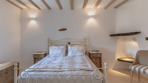Quarto com cama, mesas de cabeceira, uma cadeira e um abajur fixado na parede.