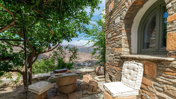 Um edifício de pedra com uma janela, uma poltrona estofada, uma mesa pequena e vista para um vale.